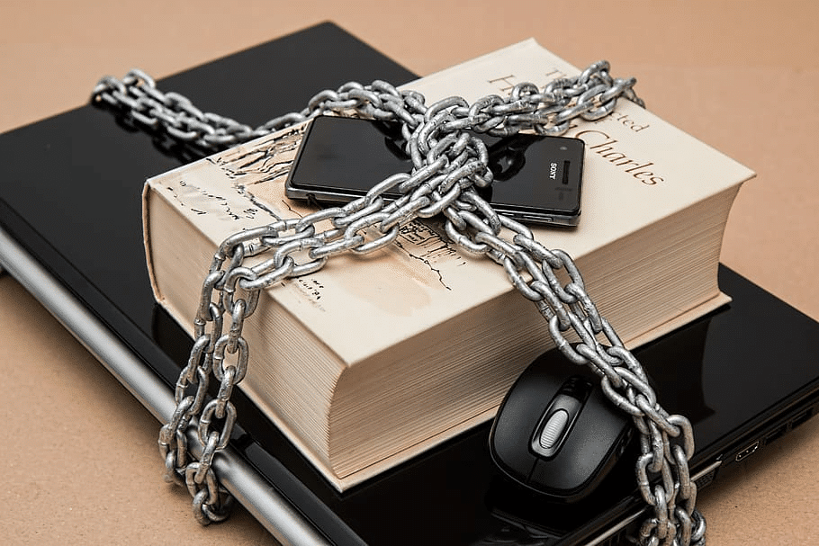 A laptop, book, cell phone, and computer mouse tied together with a heavy silver chain.